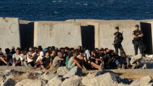 A large group of migrants are guarded by a Spanish solider